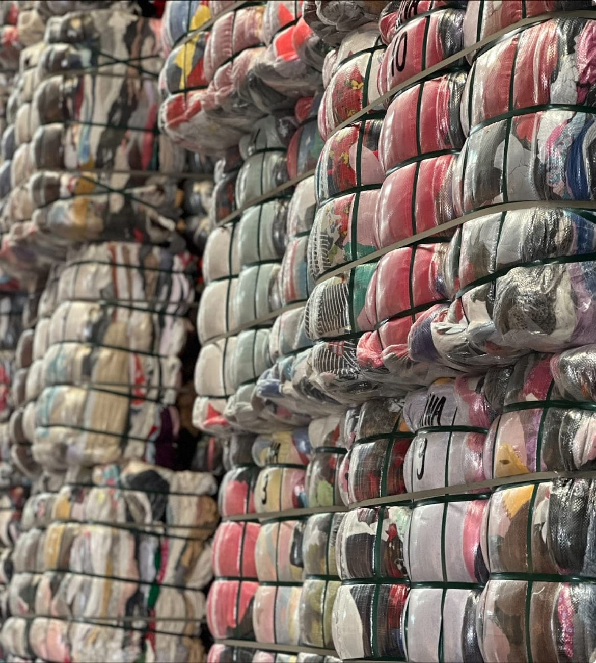 Compressed bales of used clothes stacked in a warehouse and wrapped in clear plastic.