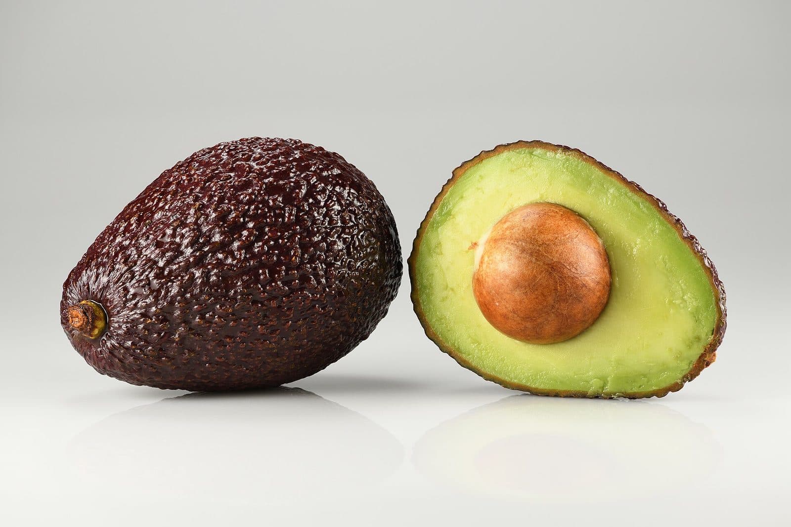 A whole Hass avocado beside one cut in half, pit still in.