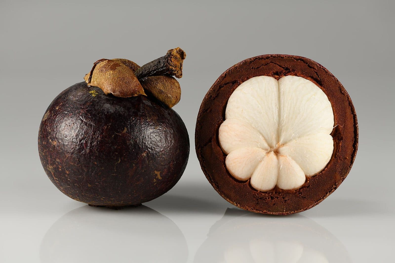 Whole mangosteens beside one opened to show the white flesh.